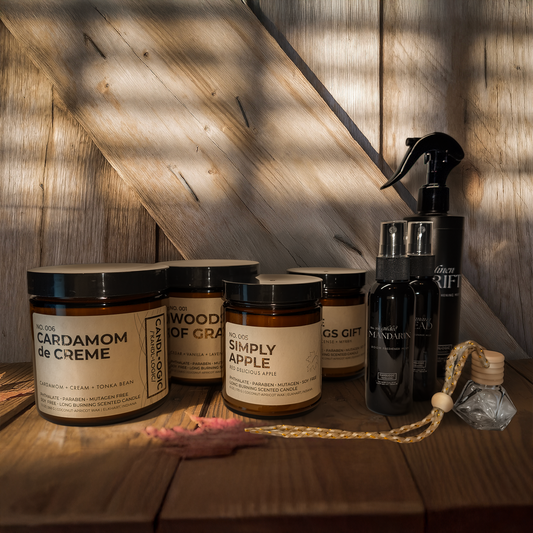 Collection of candles and a room spray bottle and a car diffuser on a wooden surface with a wooden wall background