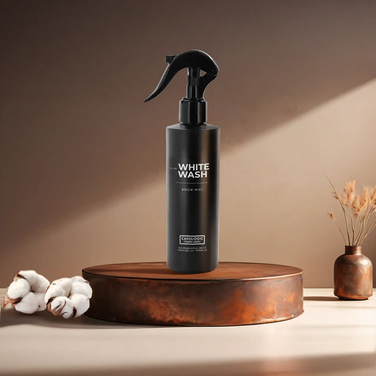 Candl•ogic’s 8 oz. room mist in a black spray bottle labeled ‘No. 019 White Wash’ on a copper tray with cotton flower stems and a copper vase in the background.