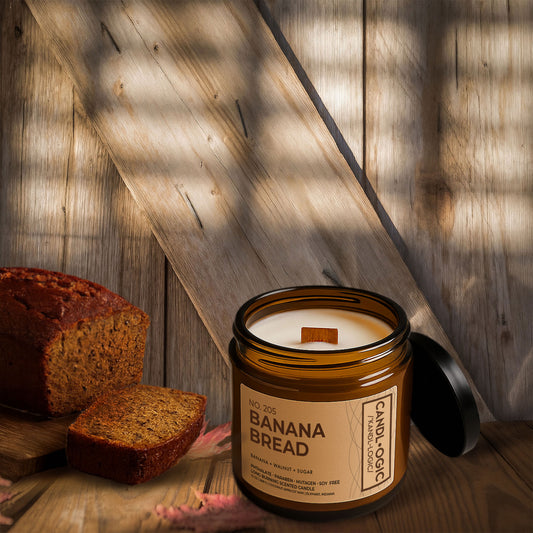 Luxury amber jar candle No. 205 Banana Bread by Candl•ogic, with banana, walnut, and sugar fragrance, displayed on rustic wooden background beside a fresh loaf of banana bread and sliced piece.