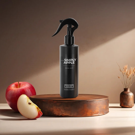 Candl•ogic’s 8 oz. room mist in a black spray bottle labeled ‘No. 005 Simply Apple’ on a copper tray with an apple and a slice of apple and a copper vase in the background.