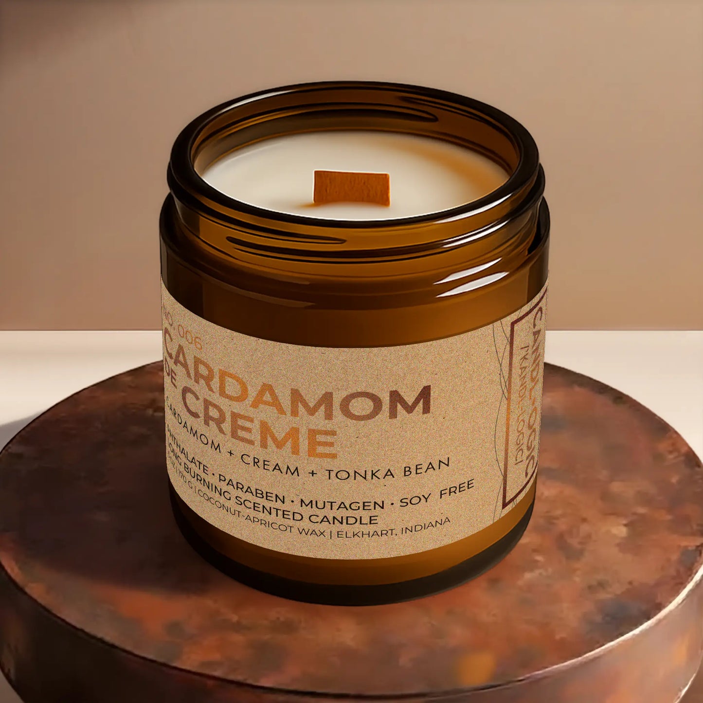 Candl•ogic’s scented candle with a wood wick viewed from the top in an amber glass 16 oz. jar labeled ‘No. 006 Cardamom de Creme’ on a copper tray.
