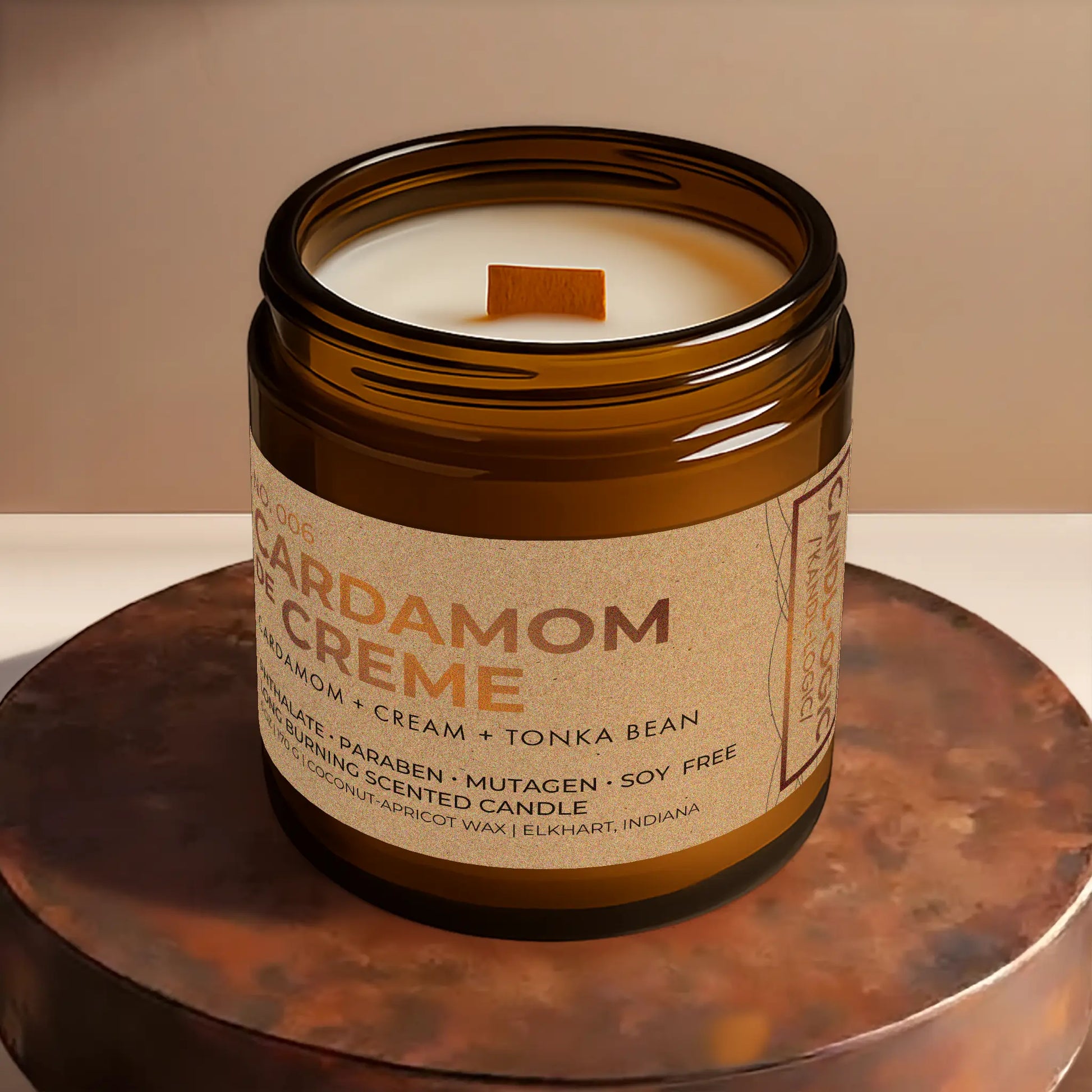 Candl•ogic’s scented candle with a wood wick viewed from the top in an amber glass 16 oz. jar labeled ‘No. 006 Cardamom de Creme’ on a copper tray.
