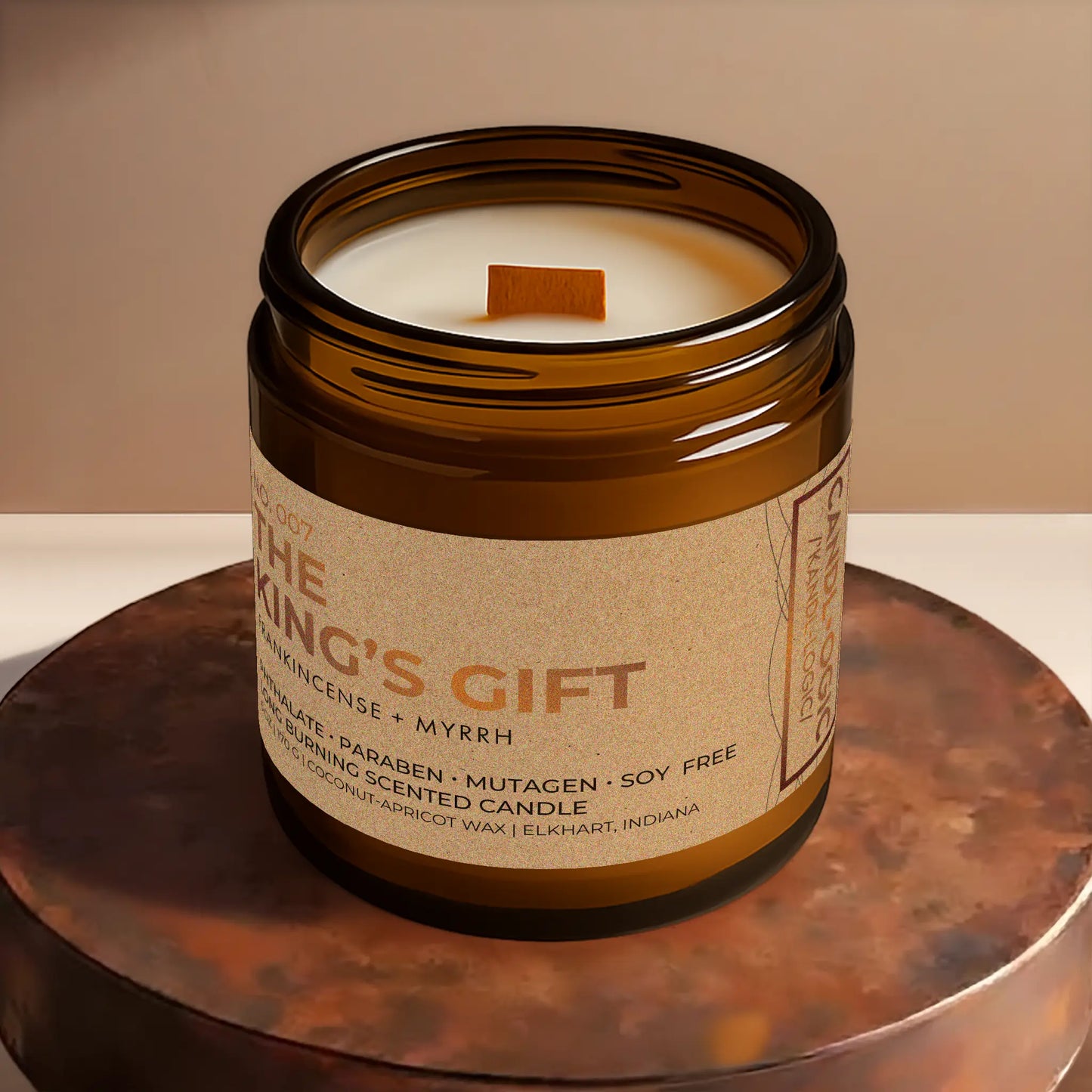 Candl•ogic’s scented candle with a wood wick viewed from the top in an amber glass 16 oz. jar labeled ‘No. 007 The King’s Gift’ on a copper tray.