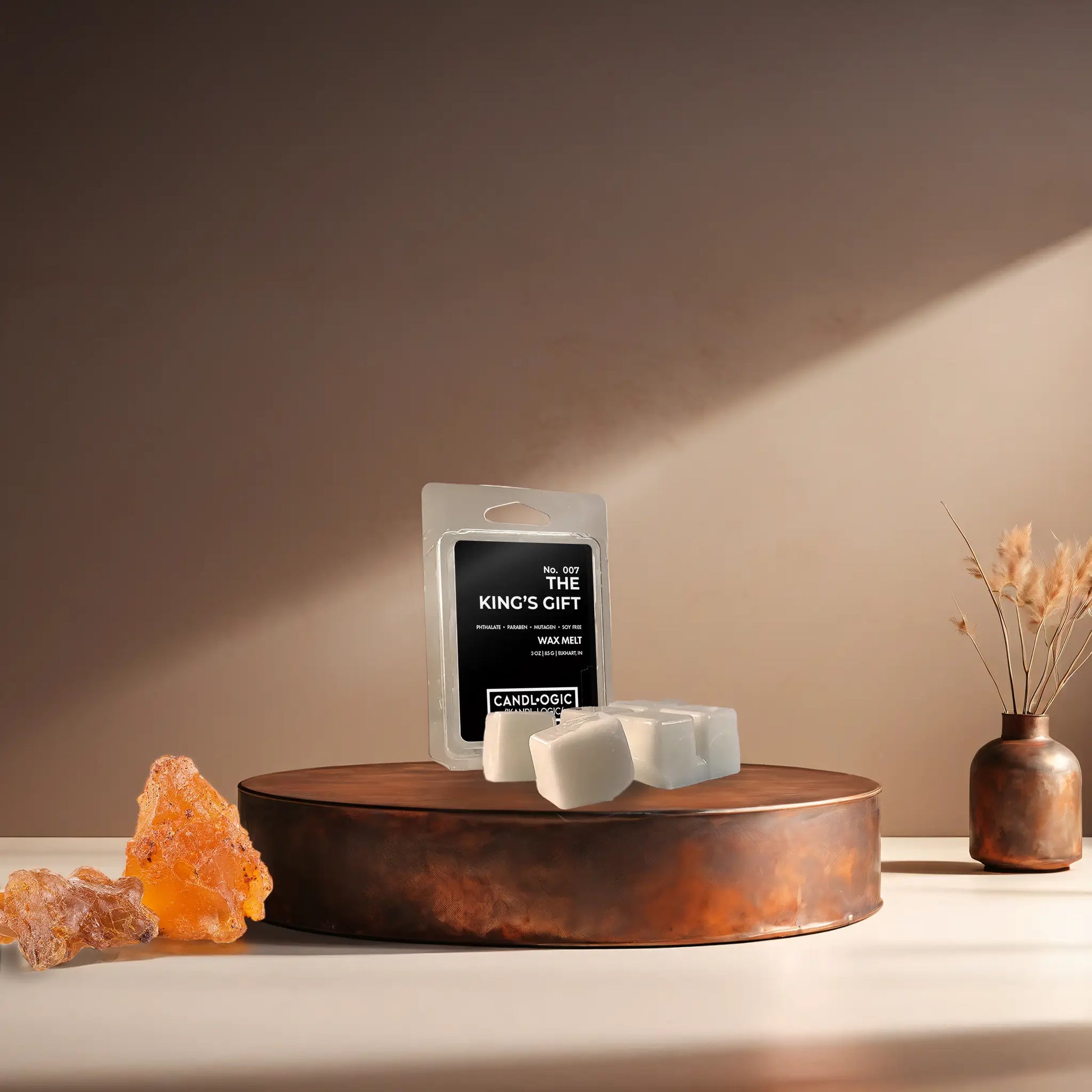 Candl•ogic’s wax melt cubes with packaging labeled ‘No. 007 The King’s Gift’ on a copper tray with frankincense and myrrh and a copper vase in the background.