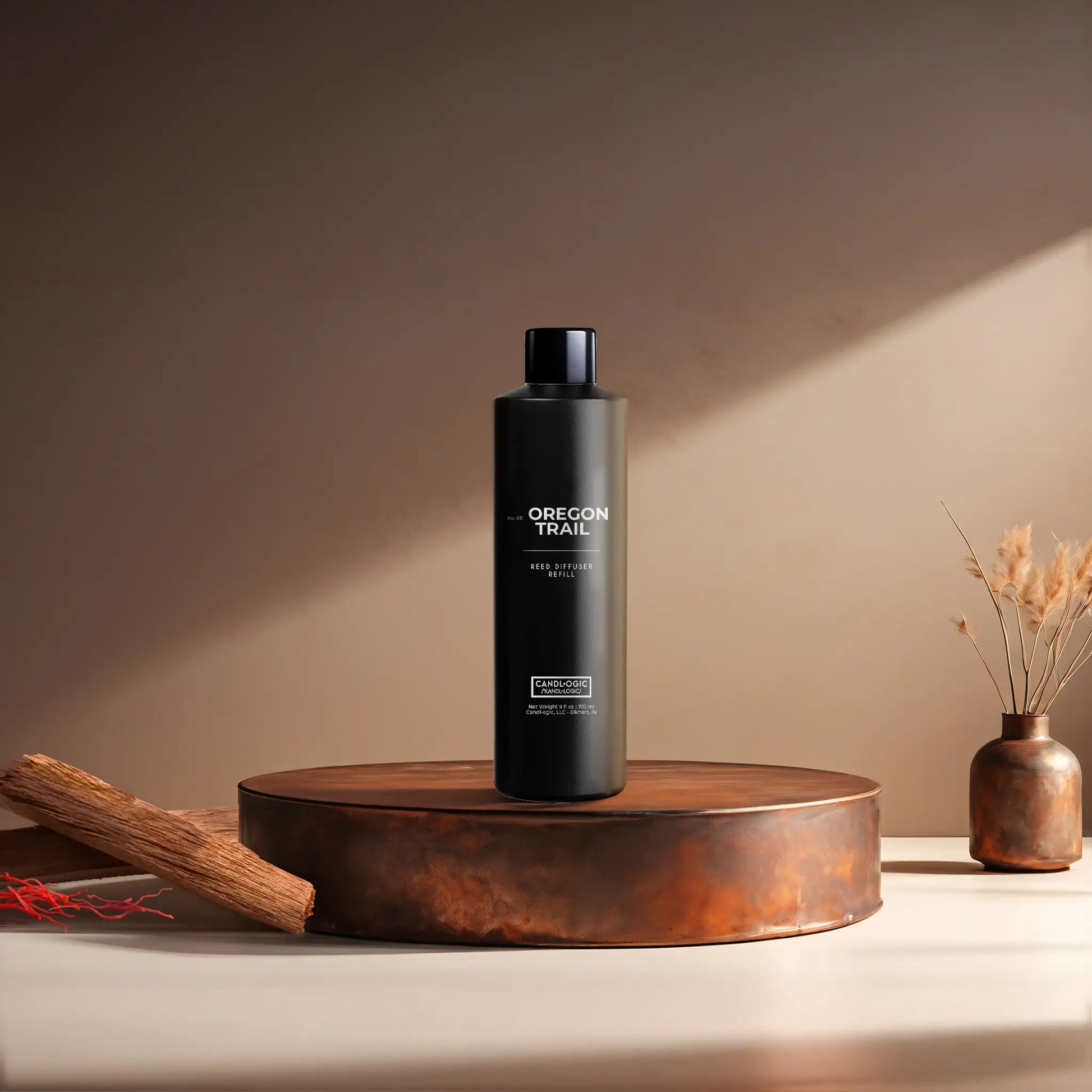 Candl•ogic’s 6 oz. reed diffuser refill solution in a black plastic bottle labeled ‘No. 011 Oregon Trail’ on a copper tray with pieces of sandalwood and strands of saffon and a copper vase in the background.