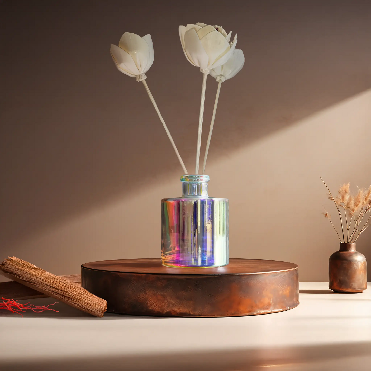Candl•ogic’s reed diffuser set in an iridescent jar with rattan flower diffuser reeds for ‘No. 011 Oregon Trail’ on a copper tray with pieces of sandalwood and strands of saffon and a copper vase in the background.
