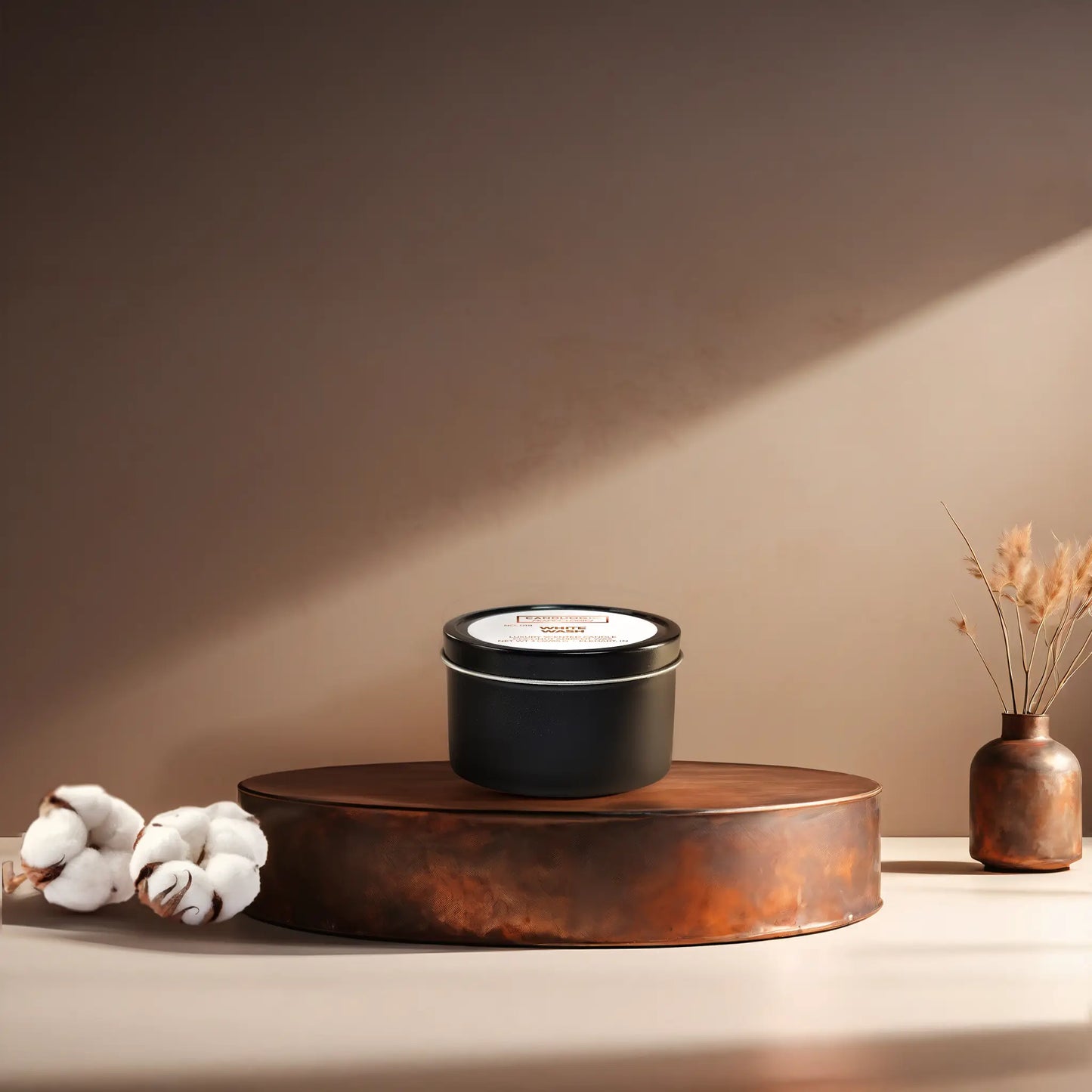 Candl•ogic’s scented candle with a wood wick in a 3 oz. black metla tin labeled ‘No. 019 White Wash’ on a copper tray with cotton flower stems and a copper vase in the background.
