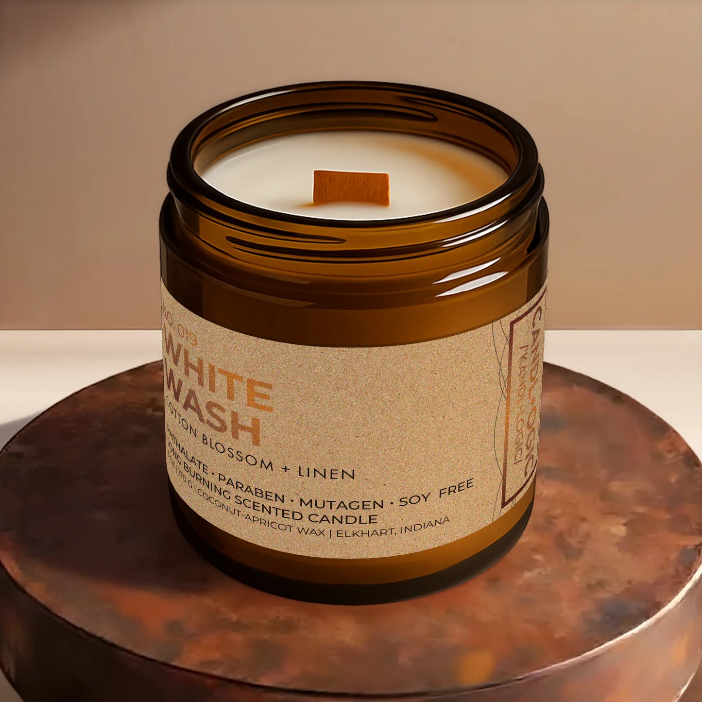 Candl•ogic’s scented candle with a wood wick viewed from the top in an amber glass 16 oz. jar labeled ‘No. 019 White Wash’ on a copper tray.