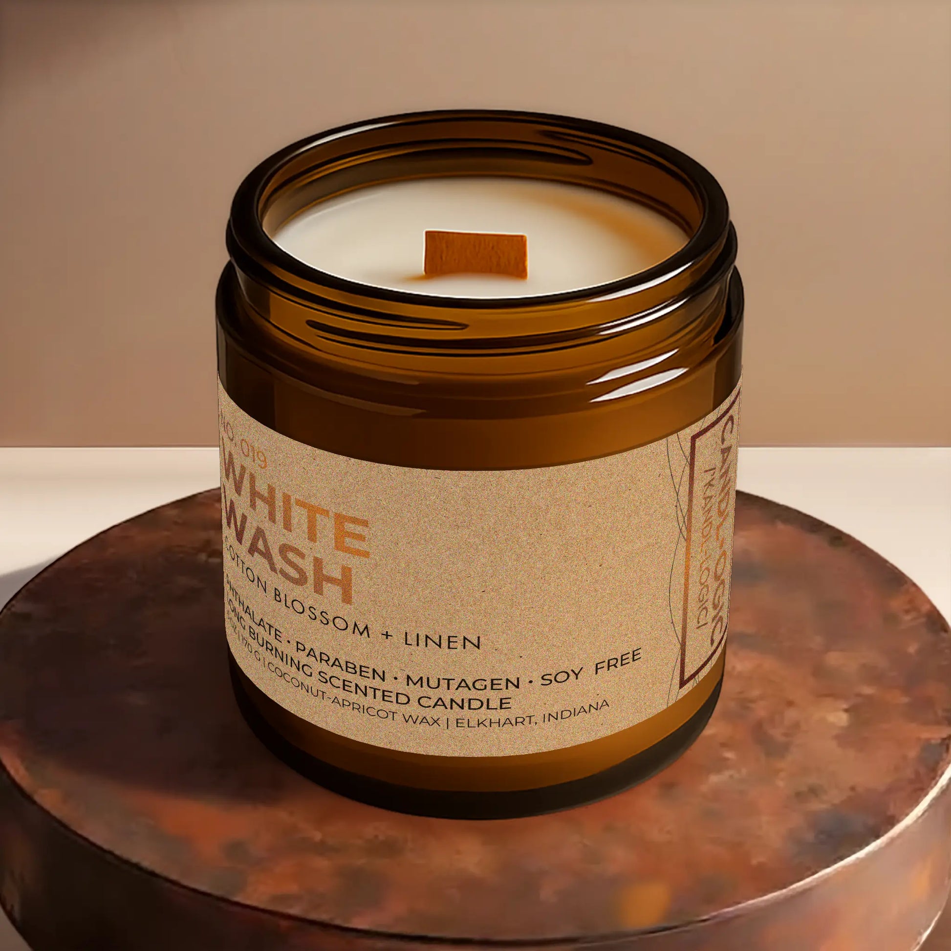 Candl•ogic’s scented candle with a wood wick viewed from the top in an amber glass 16 oz. jar labeled ‘No. 019 White Wash’ on a copper tray.