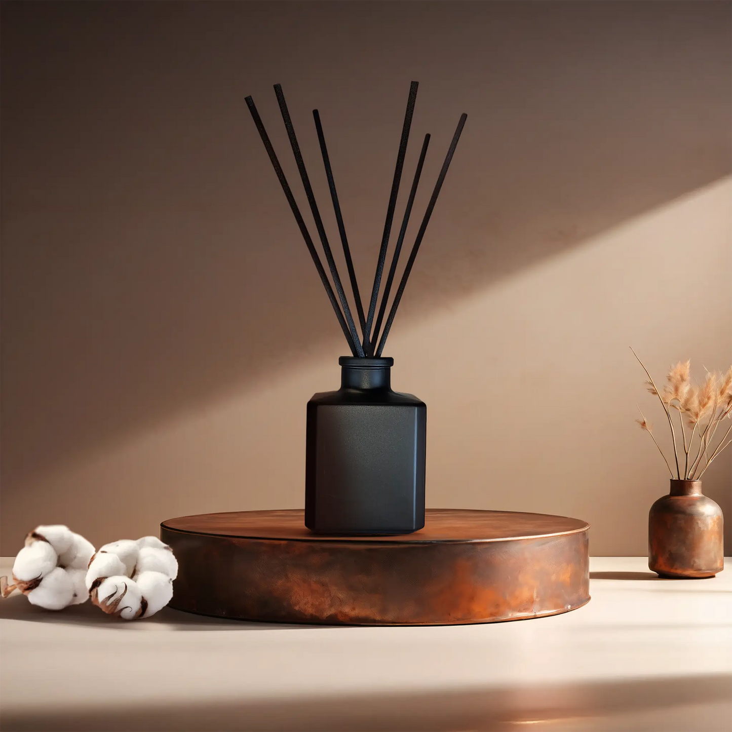 Candl•ogic’s reed diffuser set in asmall black glass cube with black fiber diffuser reeds for ‘No. 019 White Wash’ on a copper tray with cotton flower stems and a copper vase in the background.