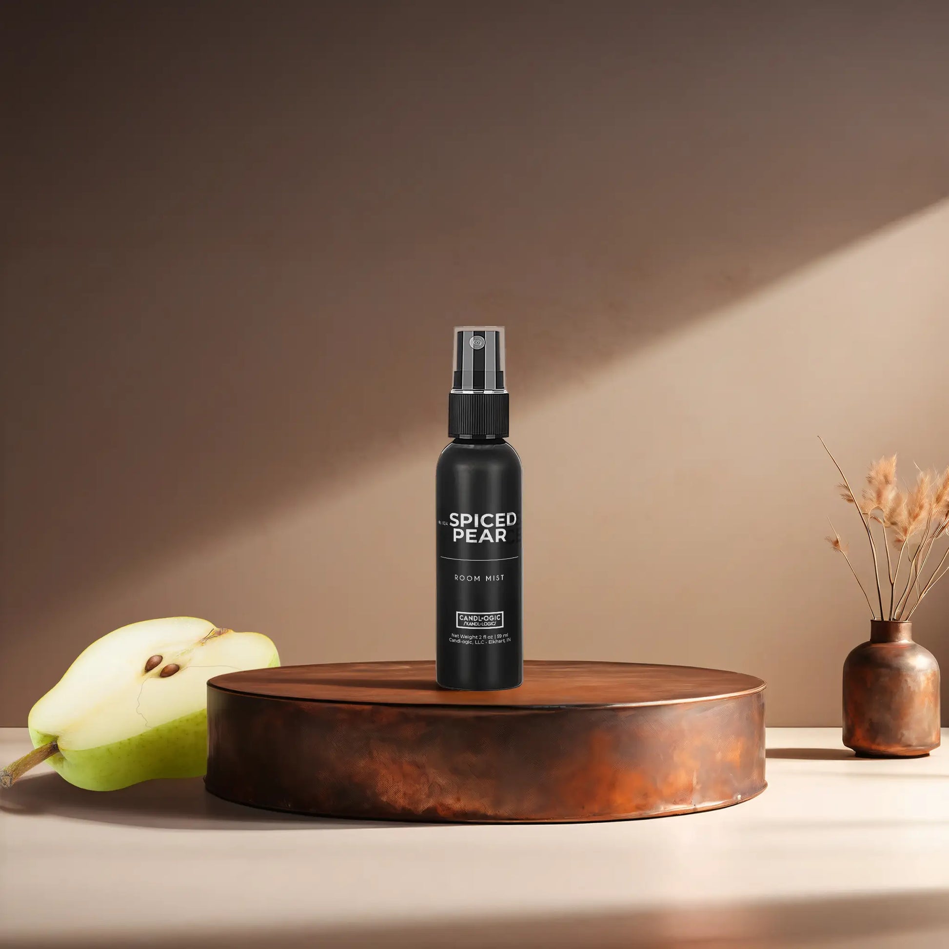 Candl•ogic’s 2 oz. room mist in a black spray bottle labeled ‘No. 024 Spiced Pear’ on a copper tray with a sliced pear and a copper vase in the background.