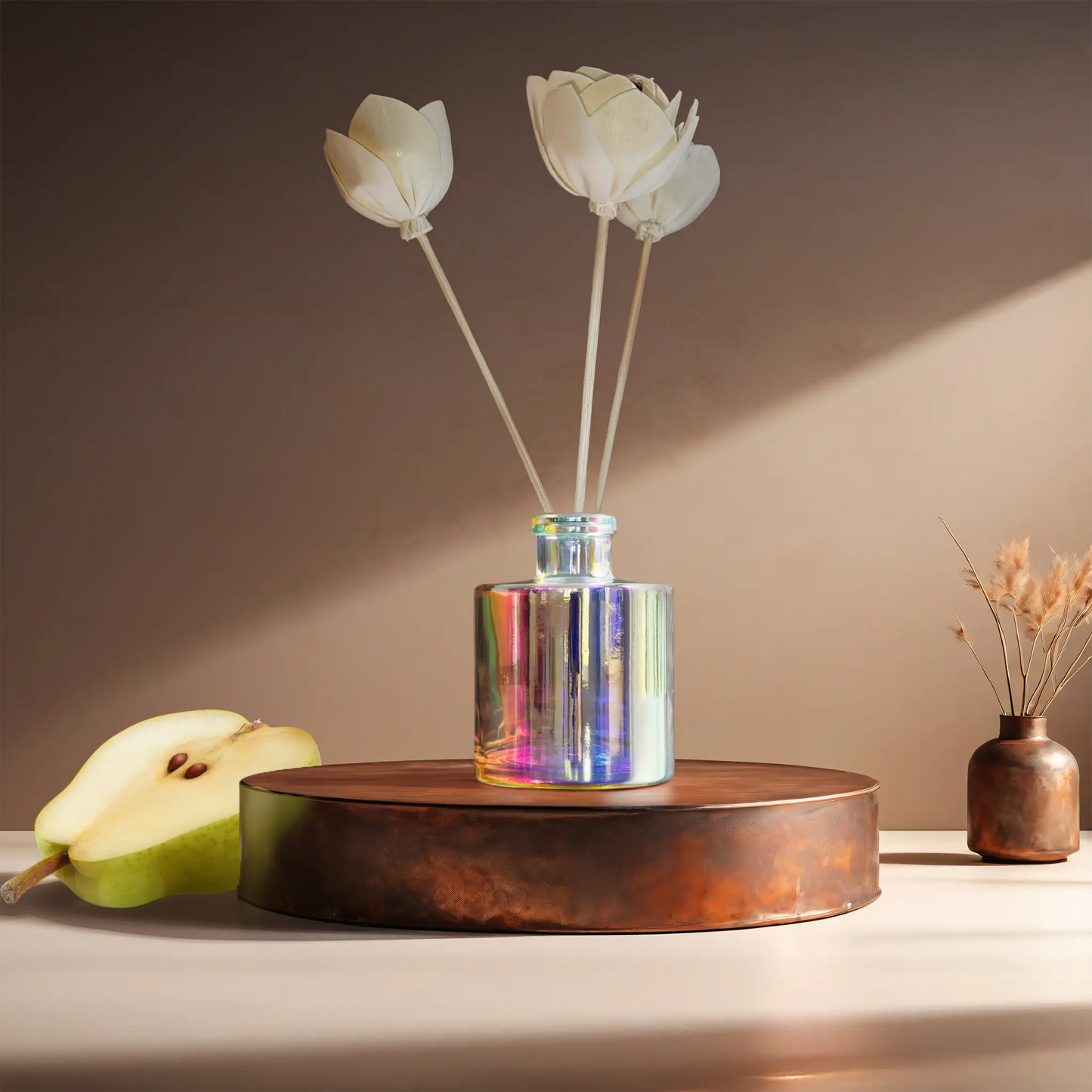 Candl•ogic’s reed diffuser set in an iridescent jar with rattan flower diffuser reeds for ‘No. 024 Spiced Pear’ on a copper tray with a sliced pear and a copper vase in the background.