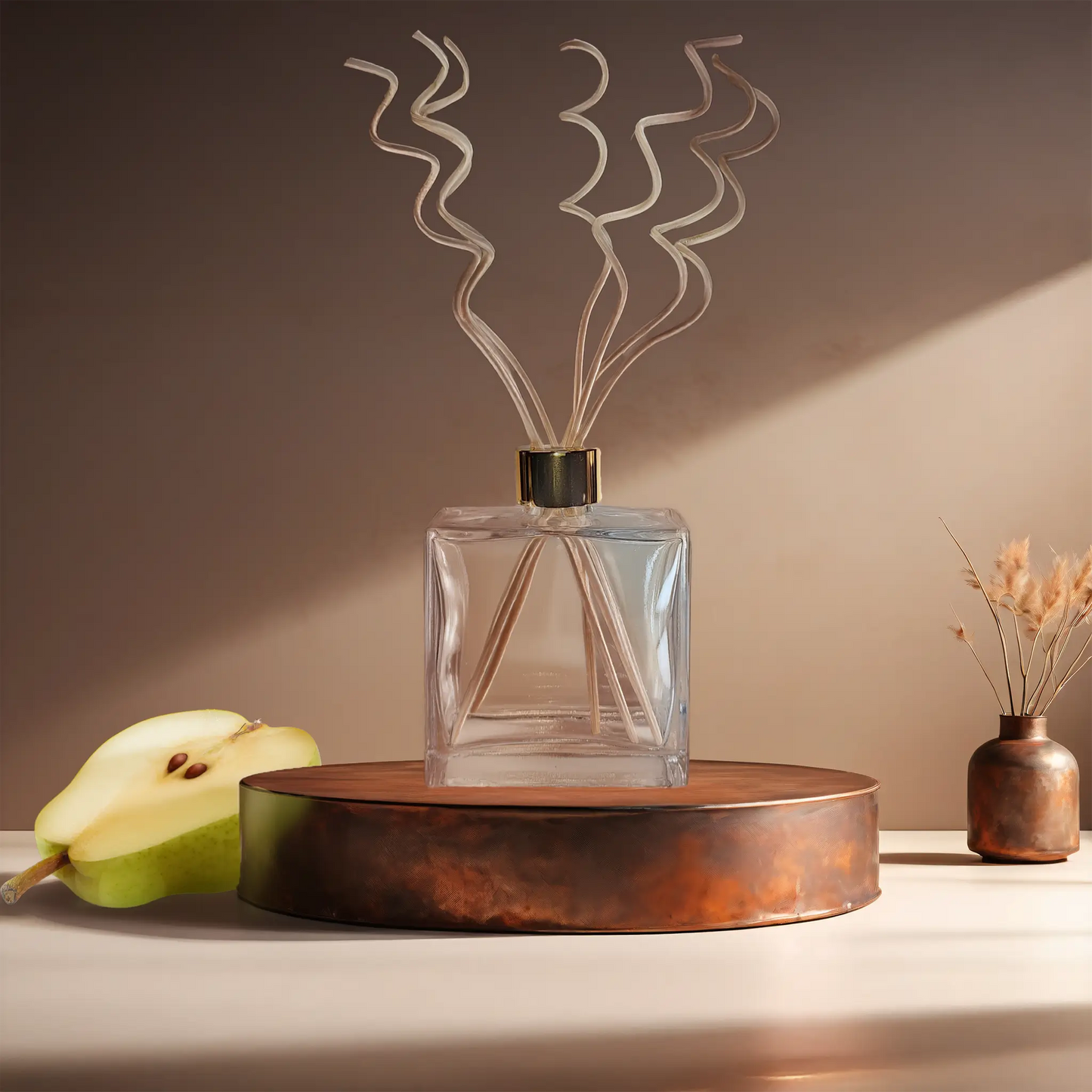 Candl•ogic’s reed diffuser set in a rectangular clear glass jar with rattan sprial diffuser reeds for ‘No. 024 Spiced Pear’ on a copper tray with a sliced pear and a copper vase in the background.