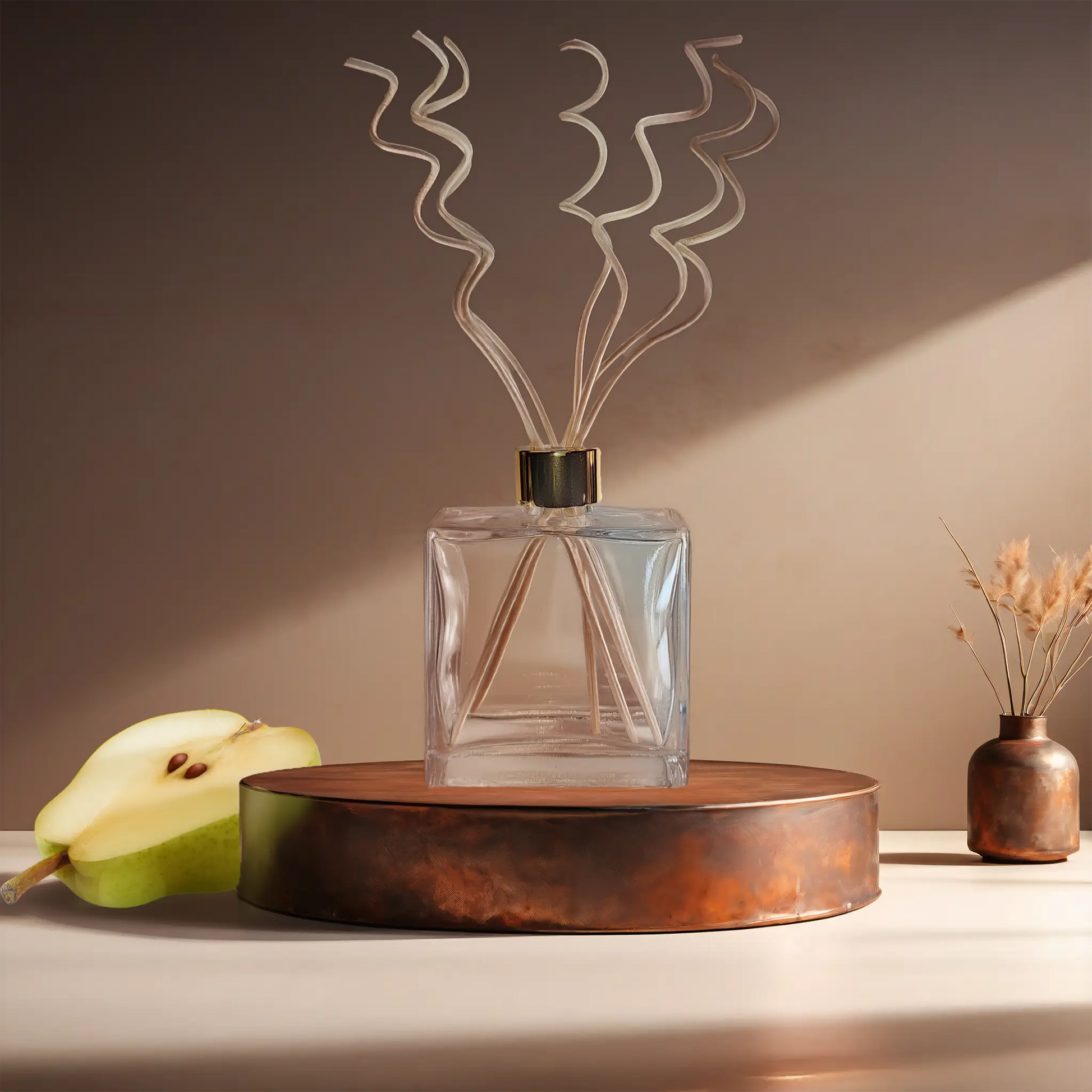 Candl•ogic’s reed diffuser set in a rectangular clear glass jar with rattan sprial diffuser reeds for ‘No. 024 Spiced Pear’ on a copper tray with a sliced pear and a copper vase in the background.