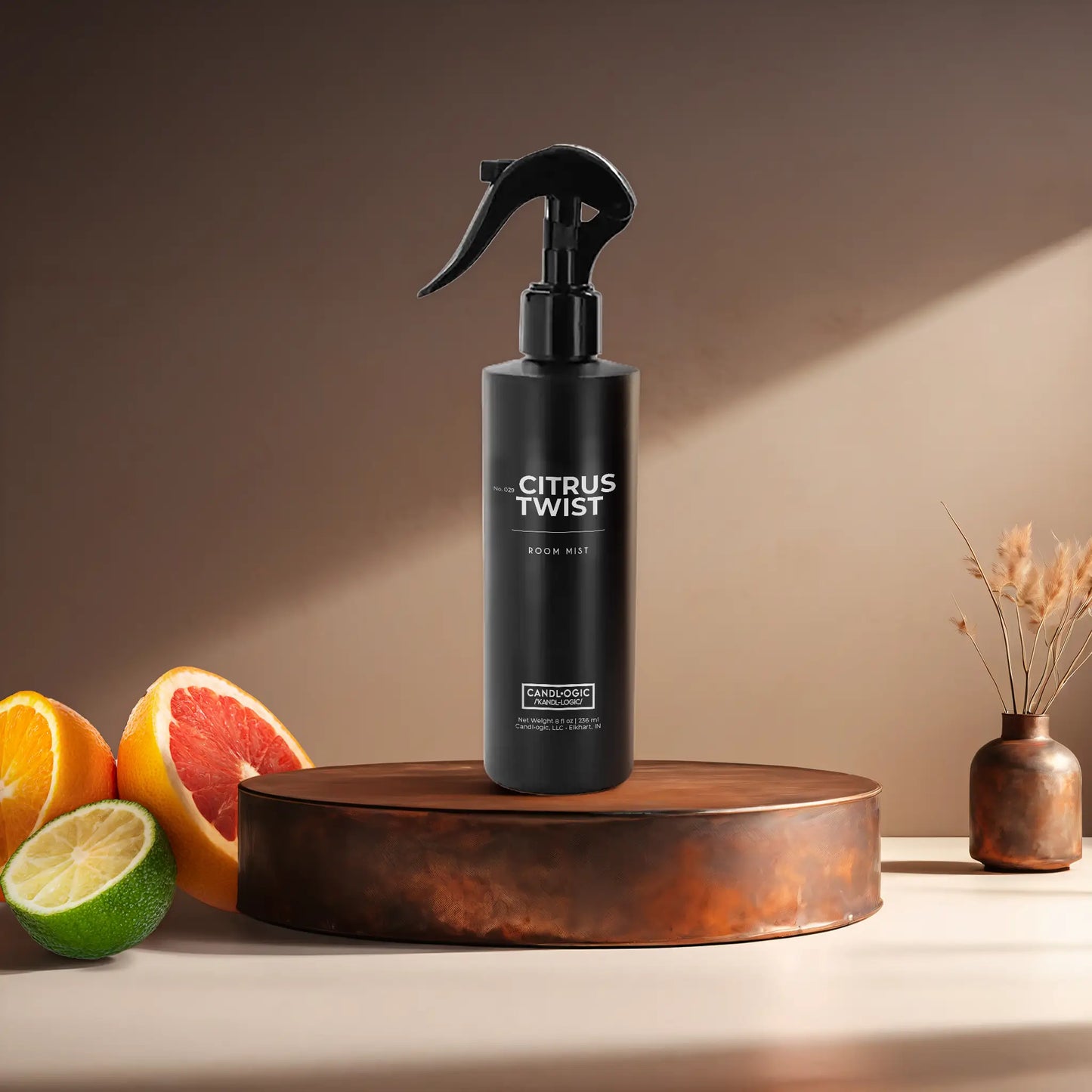 Candl•ogic’s 8 oz. room mist in a black spray bottle labeled ‘No. 029 Citrus Twist’ on a copper tray with citrus and a copper vase in the background.