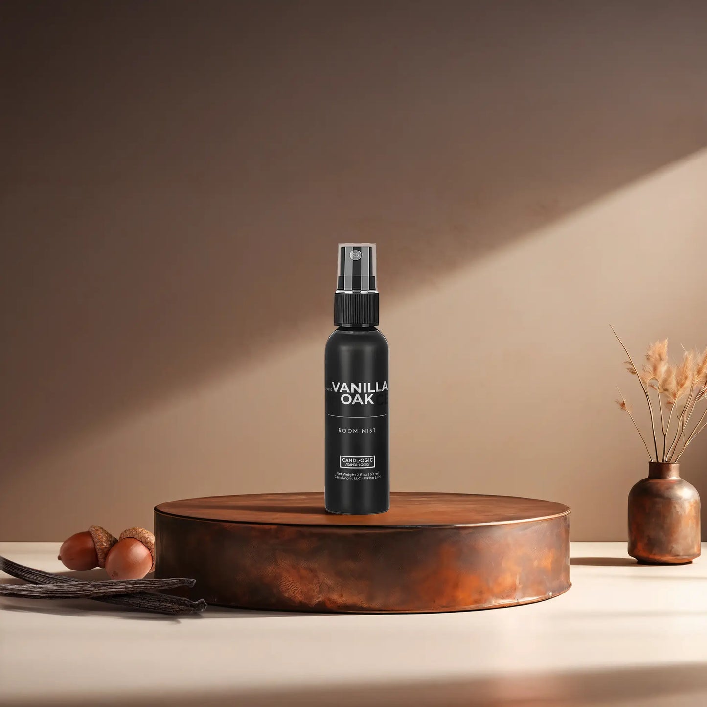 Candl•ogic’s 2 oz. room mist in a black spray bottle labeled ‘No. 034 Vanilla Oak’ on a copper tray with acorns and vanilla beans and a copper vase in the background.