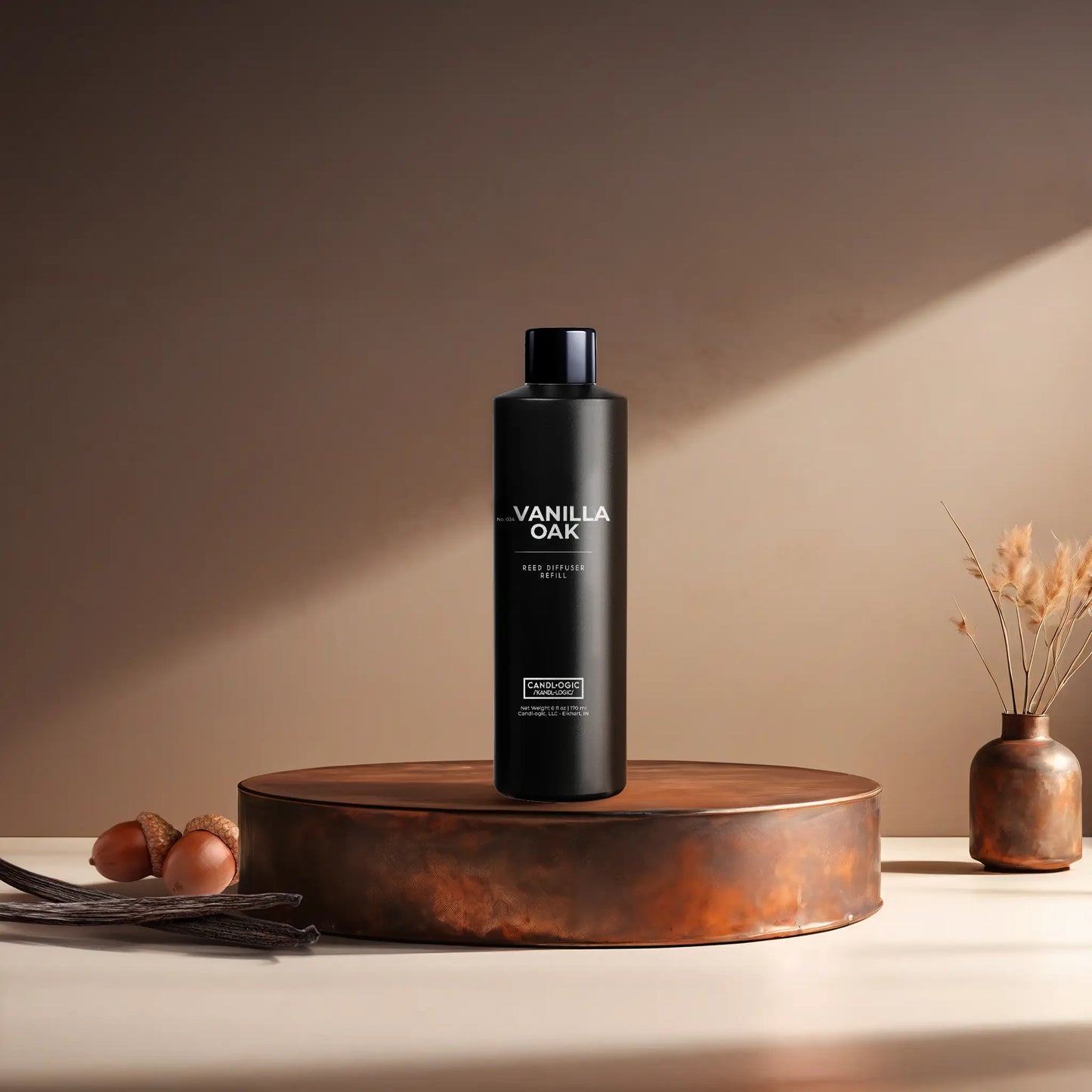 Candl•ogic’s 6 oz. reed diffuser refill solution in a black plastic bottle labeled ‘No. 034 Vanilla Oak’ on a copper tray with acorns and vanilla beans and a copper vase in the background.