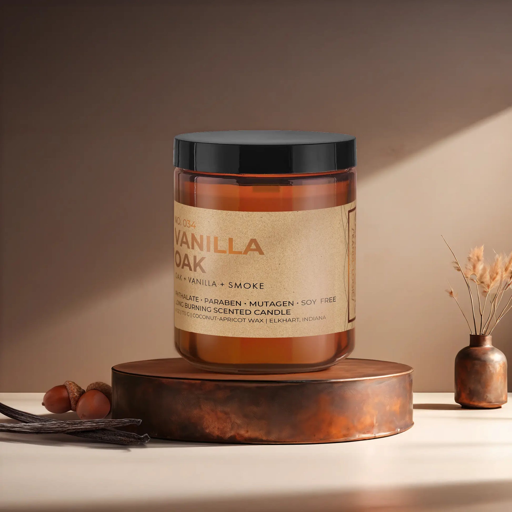 Candl•ogic’s scented candle with a wood wick in an amber glass 9 oz. jar labeled ‘No. 034 Vanilla Oak’ on a copper tray with acorns and vanilla beans and a copper vase in the background.