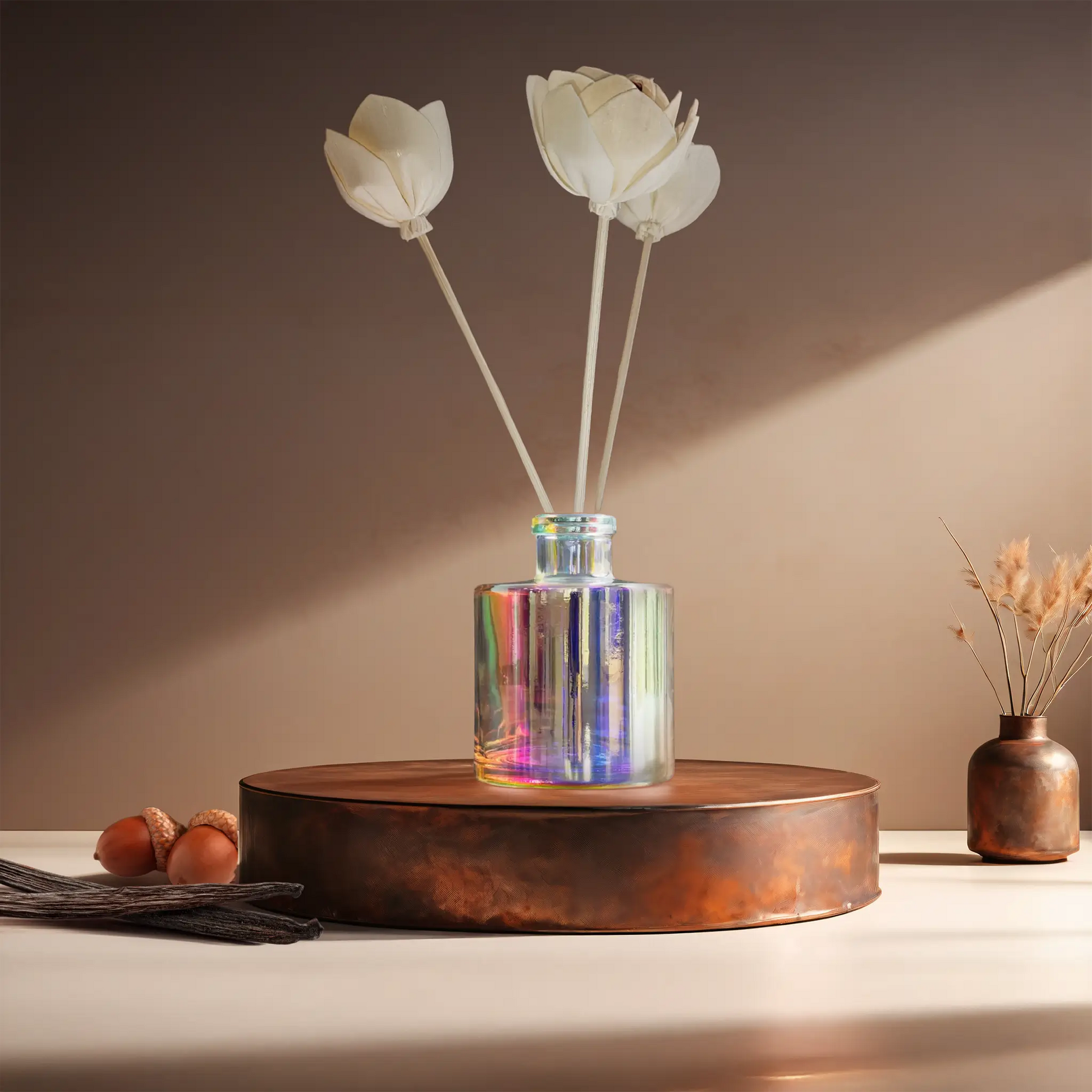 Candl•ogic’s reed diffuser set in an iridescent jar with rattan flower diffuser reeds for ‘No. 034 Vanilla Oak’ on a copper tray with acorns and vanilla beans and a copper vase in the background.