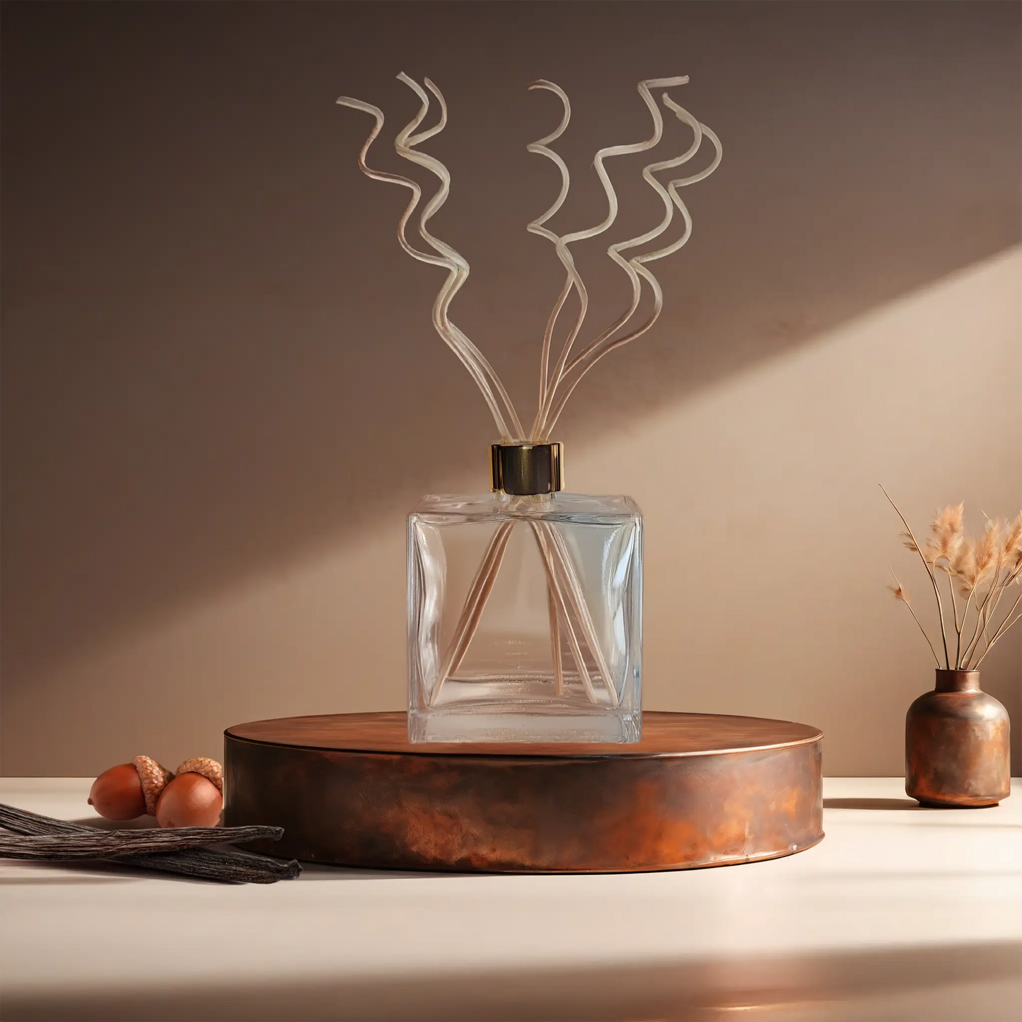 Candl•ogic’s reed diffuser set in a large rectangular clear glass jar with rattan spiral diffuser reeds for ‘No. 034 Vanilla Oak’ on a copper tray with acorns and vanilla beans and a copper vase in the background.