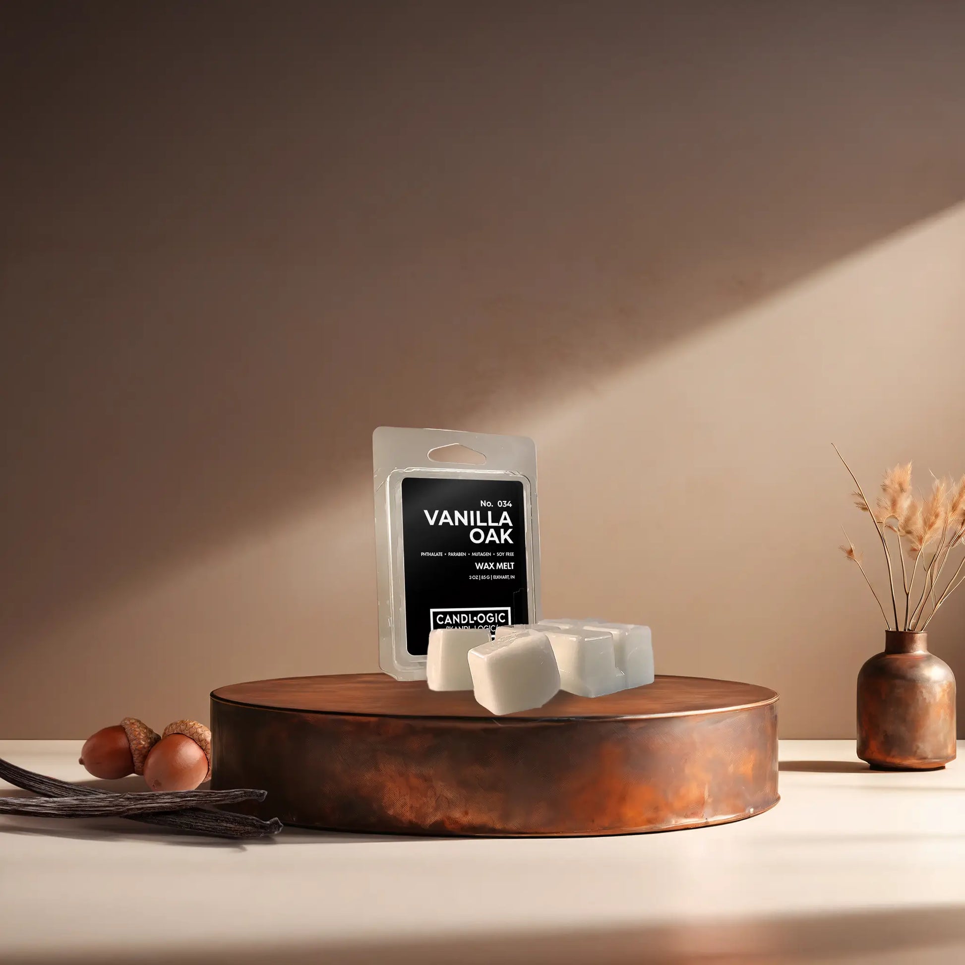 Candl•ogic’s wax melt cubes with packaging labeled ‘No. 034 Vanilla Oak’ on a copper tray with acorns and vanilla beans and a copper vase in the background.