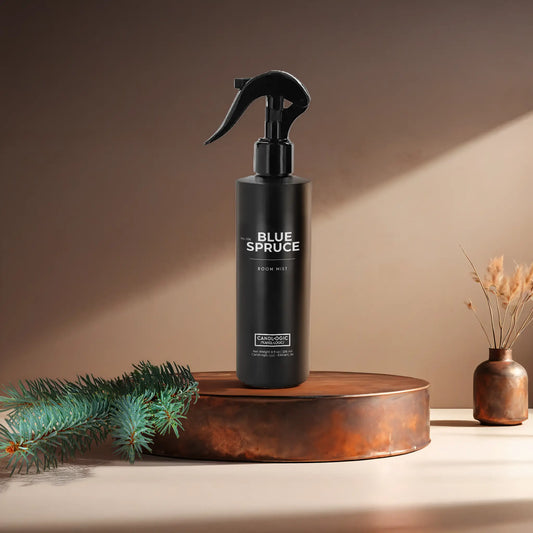 Candl•ogic's 8 oz. room mist in a black spray bottle labeled 'No. 036 Blue Spruce' on a copper tray with a blue spruce bough and a copper vase in the background