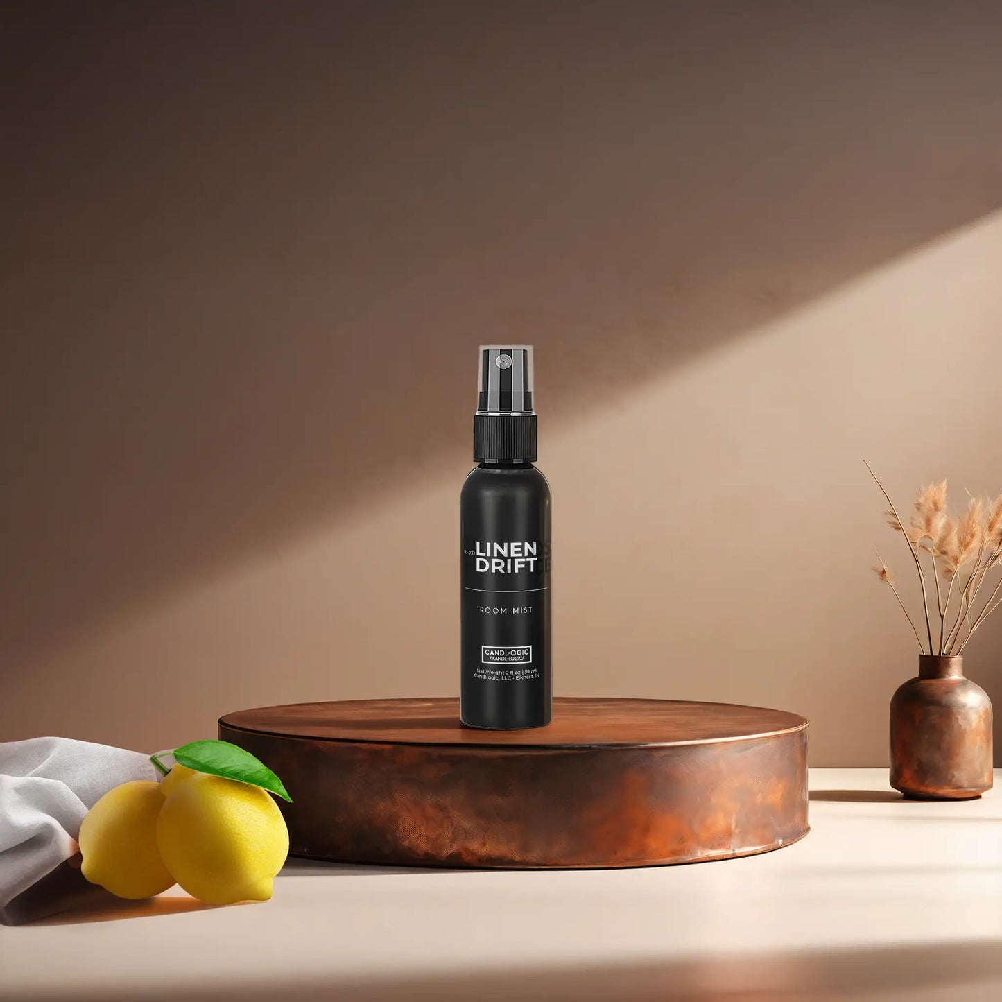 Candl•ogic's 2 oz. room mist in a black spray bottle labeled 'No. 038 Linen Drift' on a copper tray with a white fabric piece and lemons and a vase in the background.