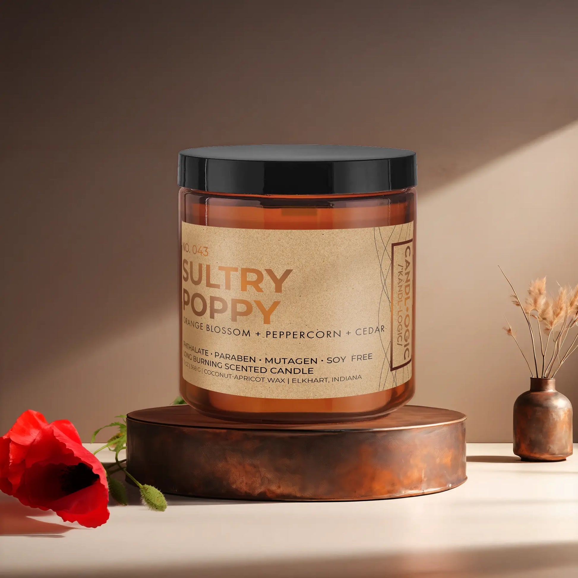Candl•ogic's scented candle with a wood wick in an amber glass 16 oz. jar labeled 'No. 043 Sultry Poppy' on a copper tray with a red poppy flower and a vase in the background.