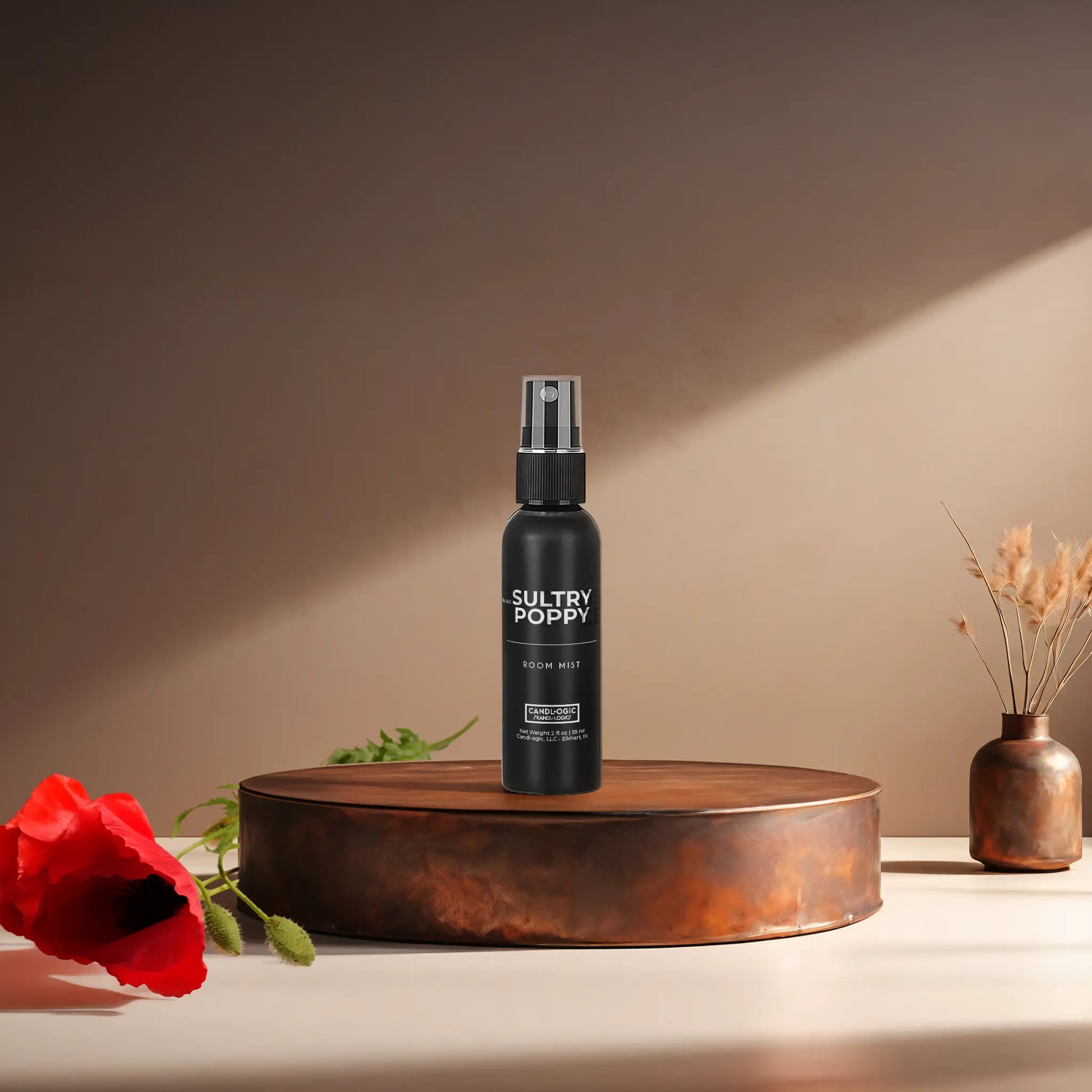 Candl•ogic's 2 oz. room mist in a black spray bottle labeled 'No. 043 Sultry Poppy' on a copper tray with a red poppy flower and a vase in the background.