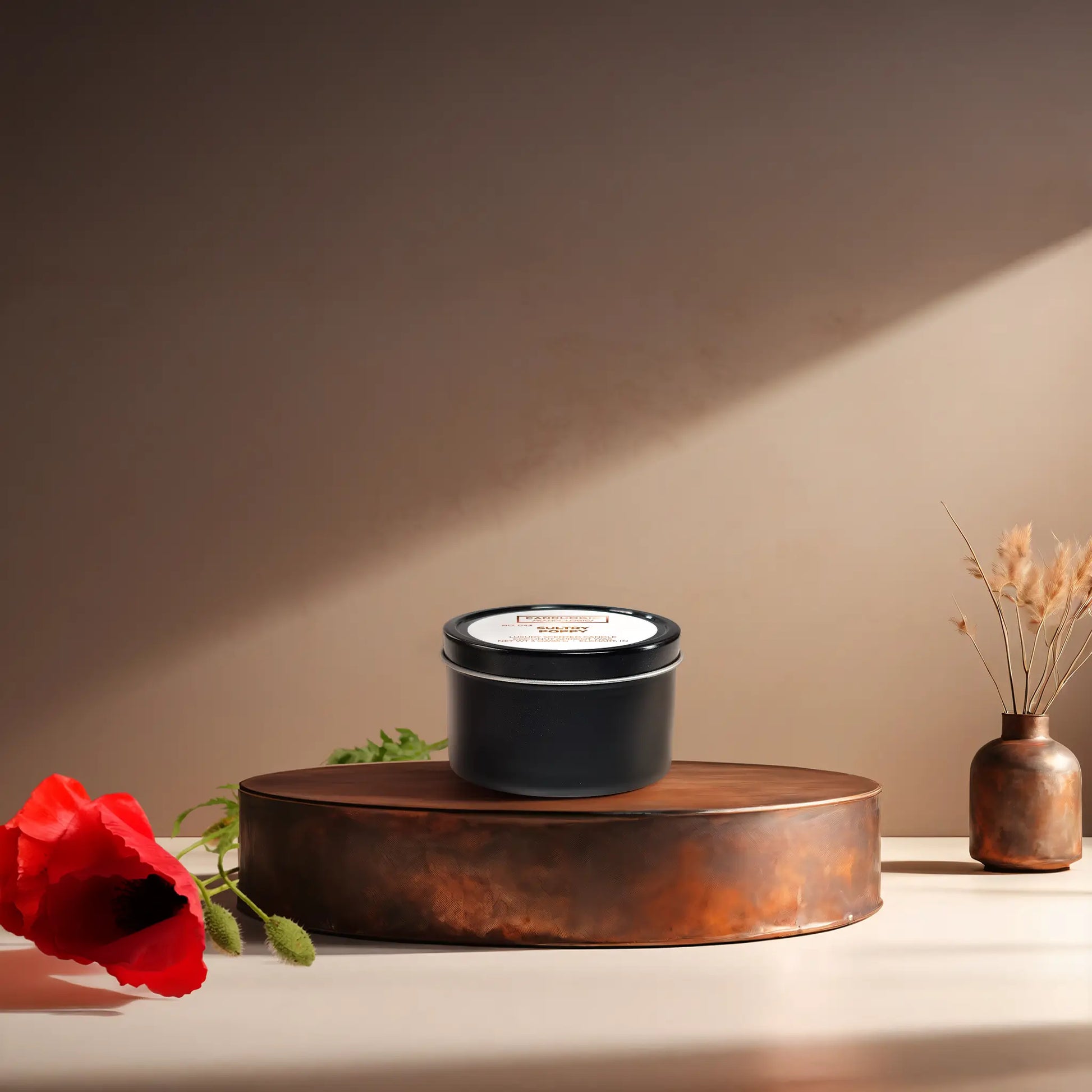 Candl•ogic's scented candle with a wood wick in a 3 oz. black metal tin labeled 'No. 043 Sultry Poppy' on a copper tray with a red poppy flower and a vase in the background.