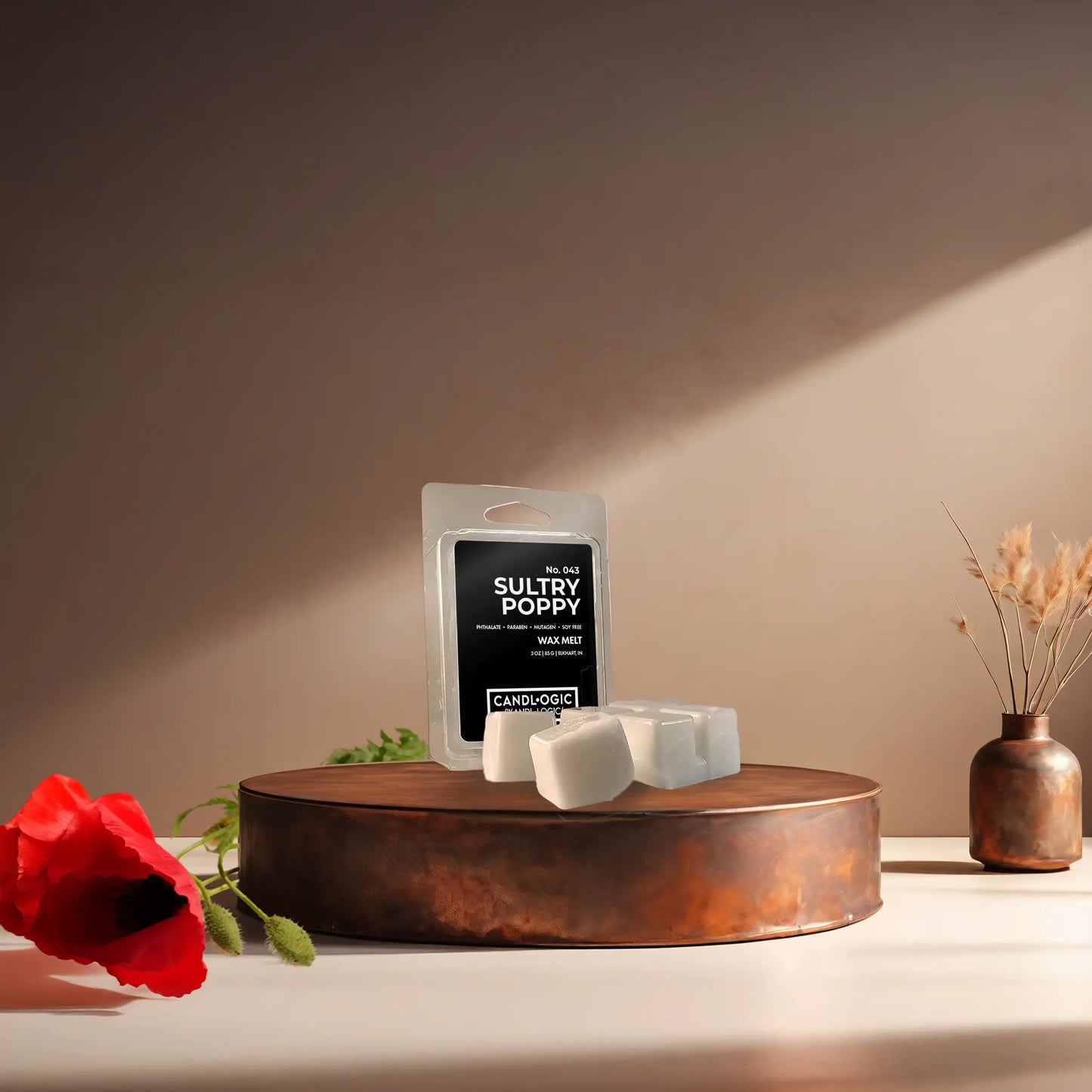 Candl•ogic's wax melt cubes and packaging labeled 'No. 043 Sultry Poppy' on a copper tray with a red poppy flower and a vase in the background.